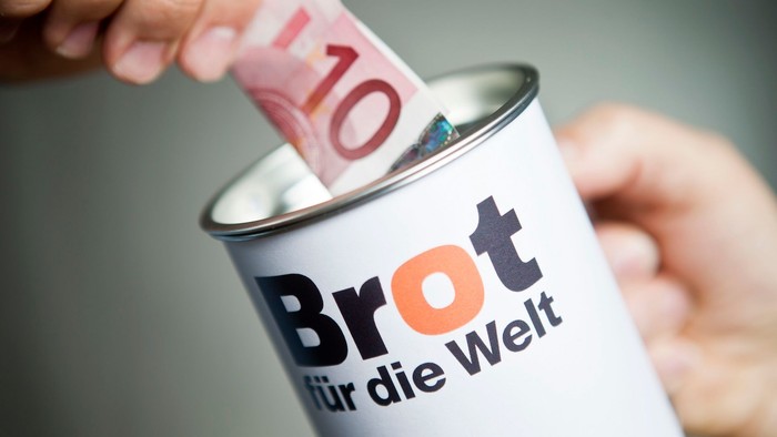 Ein Geldschein wird in eine Spendendose von Brot für die Welt gesteckt