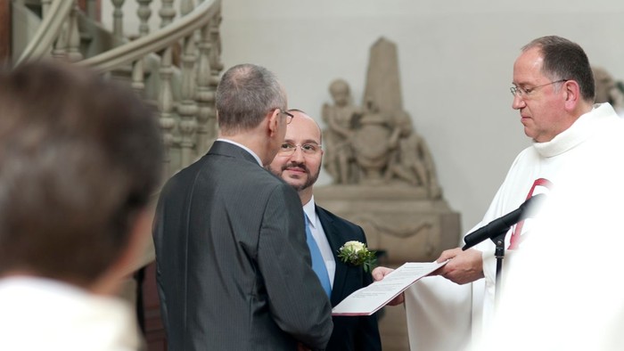Drei Männer in Anzügen bei einer Zeremonie in einer Kirche