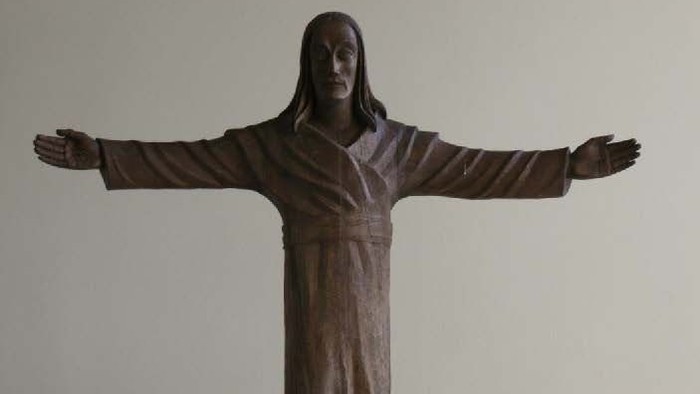 Bronzestatue Christi mit ausgebreiteten Armen auf einem Marmorsockel mit einem Kreuzsymbol.