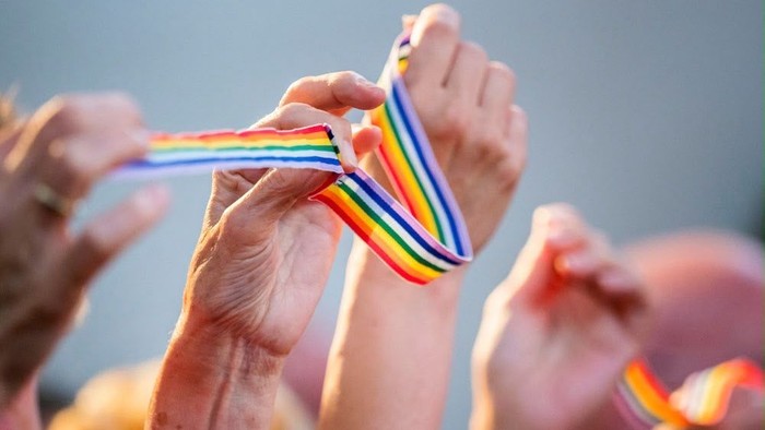 Hände, die ein regenbogenfarbenes Pride-Band halten und anpassen während einer Feier.