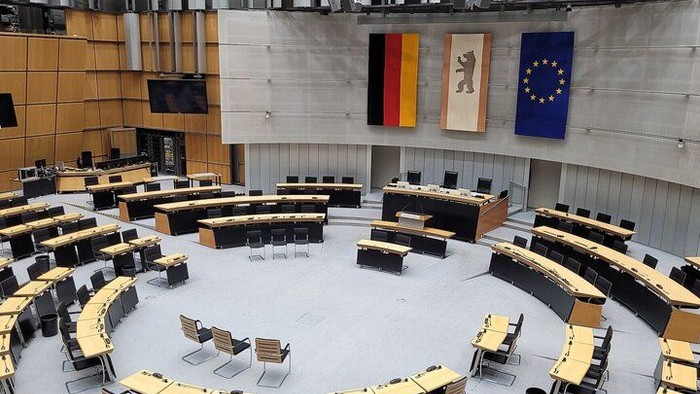 Moderner Konferenzsaal mit geschwungener Sitzanordnung, in dem deutsche und EU-Flaggen zu sehen sind.