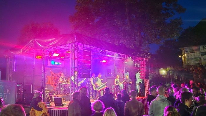 Das Bild zeigt die Bühne von Rock am Kirchberg, davor Menschen, die der Band zuhören.