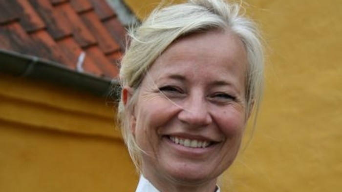 En kvinde med blond hår smiler til kameraet.