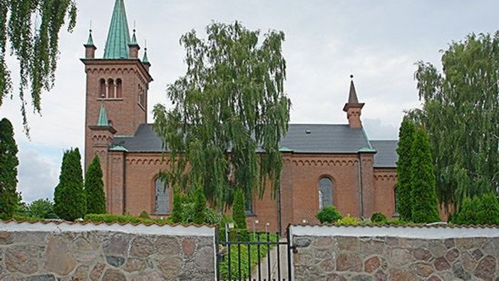 En rød murstenskirke med to tårne og grønne træer.