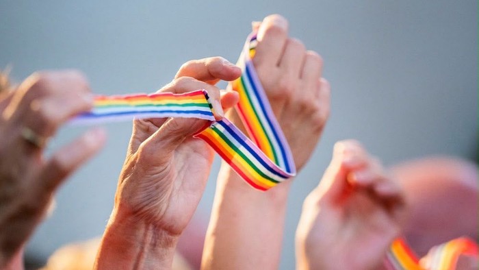 Hände halten ein Regenbogenband.