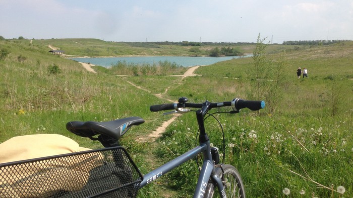 En cykel med kurv står ved en sti med udsigt over en sø og en grøn dal