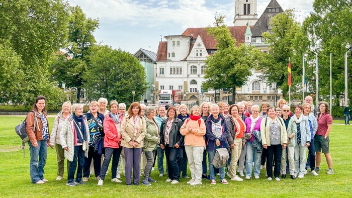 Eine große gemischte Gruppe in einem Park. Im Hintergrund eine historische Fassade und ein Glockenturm.
