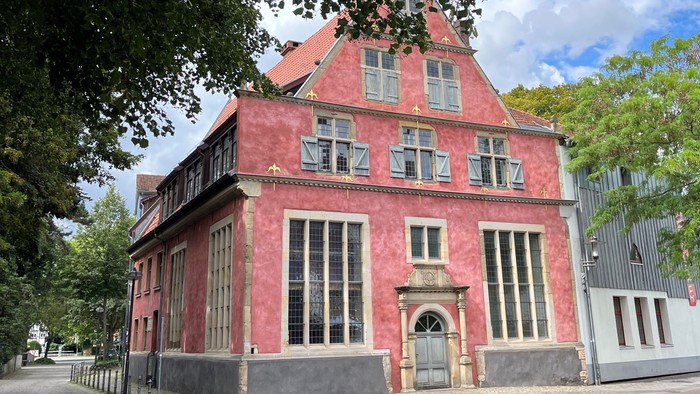 Lebhaftes rotes Backsteingebäude mit steilen Giebeln und großen Fenstern in einer Kopfsteinpflasterstraße.