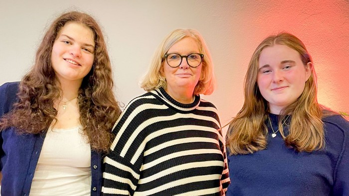 Eine Frau mit Brille und gestreiften Pullover zwischen zwei jungen Frauen mit blauen Oberteilen
