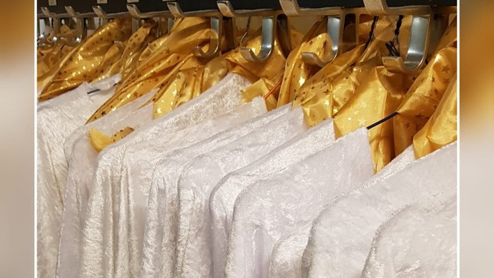 Weiße Kleider mit goldenen Bändern hängen im Laden
