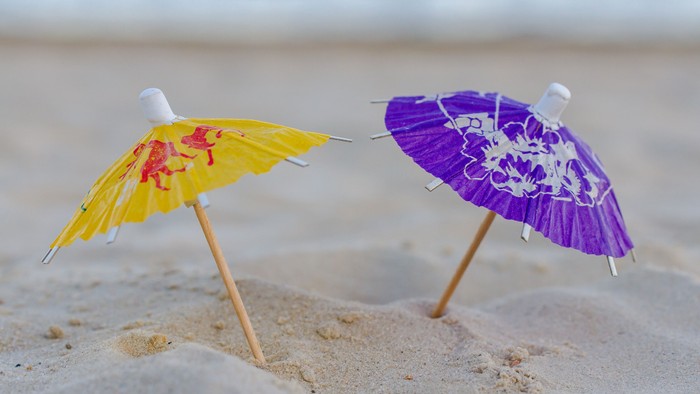 Zwei bunte Sonnenschirme stecken im Sand am Strand.