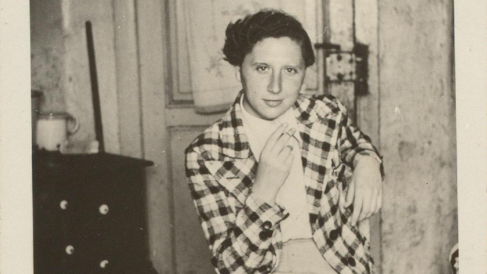 Ein vintage Schwarz-Weiß-Porträt einer Person in einem karierten Hemd, die drinnen in der Nähe einer Kommode steht.