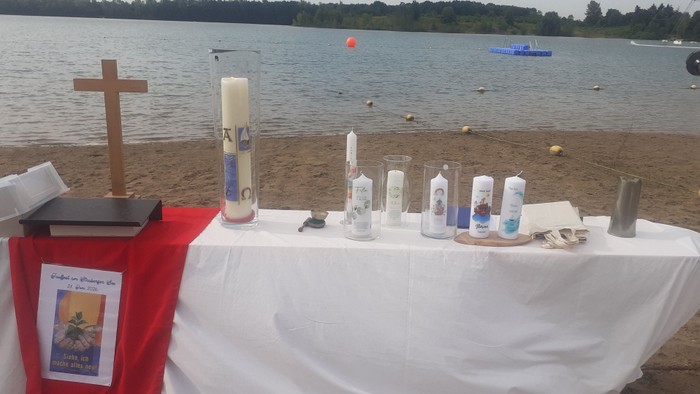 Tisch mit Kreuz, Osterkerze und Kerzen der Täuflinge. Im Hintergrund Blick auf den Straberger See.