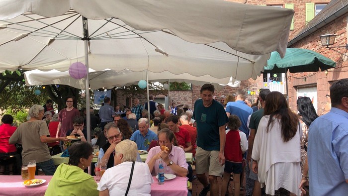 Draußen stattfindende gesellige Zusammenkunft mit Menschen, die Essen, Getränke und Gespräche unter großen Sonnenschirmen genießen.