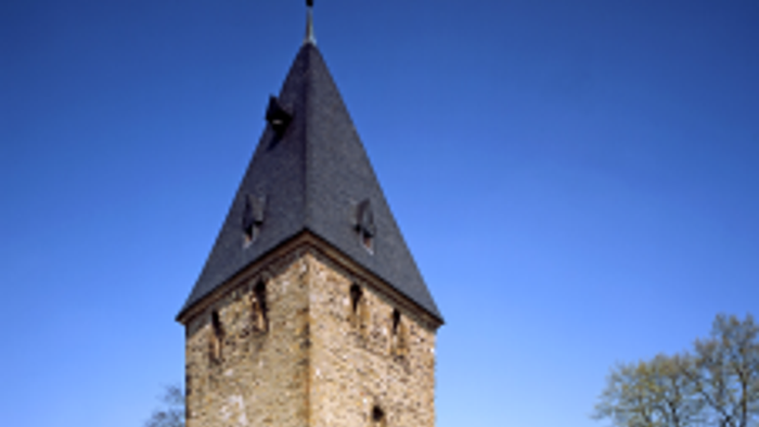 Historische Steinkirche mit hohem Glockenturm vor klarem blauem Himmel.