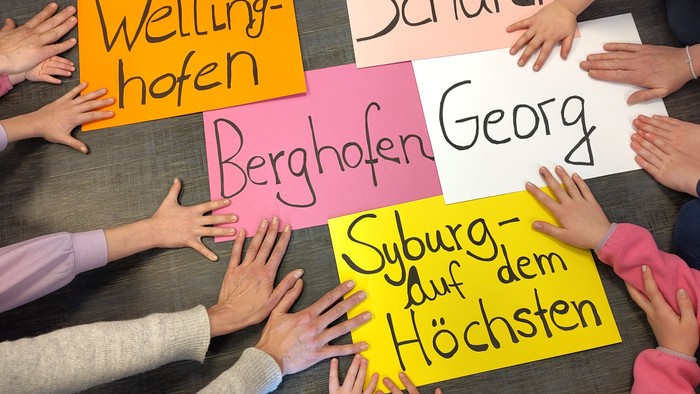 Kinder, die bunte Schilder mit deutschen Ortsnamen und Sätzen in einer Gruppenaktivität halten.