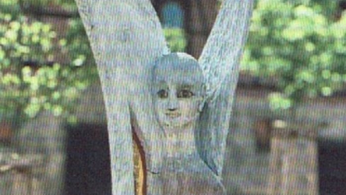 Eine hölzerne Statue eines Engels namens Michael steht friedlich in einem Garten im Freien.