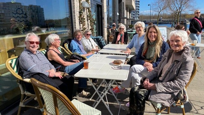 En gruppe mennesker nyder en solskinsdag udendørs på en café ved havnefronten.
