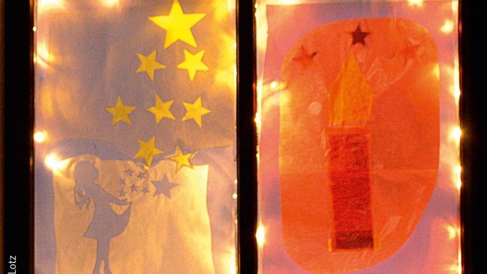 Vier beleuchtete Fenster mit Zahlen und Sternen, darunter ein Kind mit Sternen