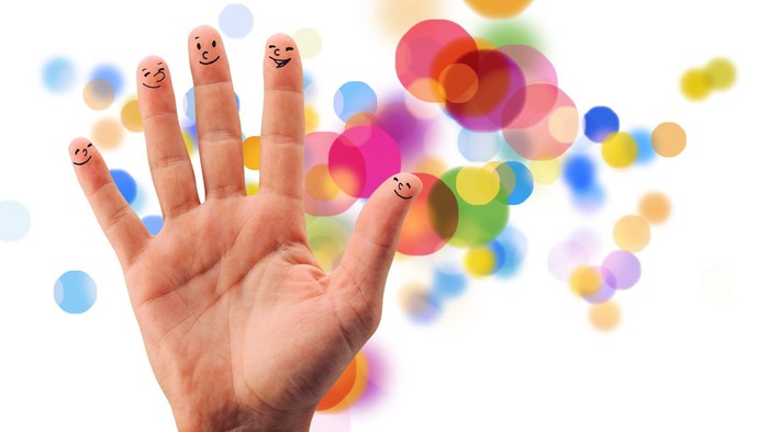 Eine fröhliche Hand mit aufgemalten Smiley-Gesichtern auf den Fingern, umgeben von bunten Konfettipunkten.