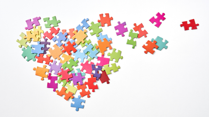 Bunte Puzzleteile, die zu einer Herzform angeordnet sind, mit einem abgetrennten Teil.