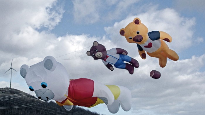 Bunte riesige Teddybär-Drachen, die verspielt am teilweise bewölkten Himmel fliegen.