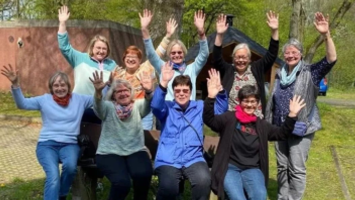 In einem Garten stehen 9 Frauen auf einem Gruppenfoto. Sie heben voller Freude die Hände in die Höhe.