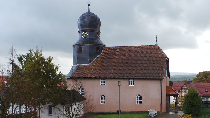 Ein Kirchengebäude mit schwarzer Kuppel und Uhr, umgeben von grünem Rasen und anderen Häusern.