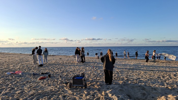Menschen versammeln sich an einem sandigen Strand nahe dem Ozean unter einem klaren Himmel während der Abenddämmerung.