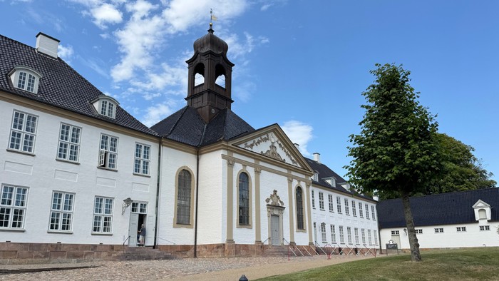 Elegant historisk bygning med et centralt klokketårn og symmetrisk hvid facade omgivet af grønne græsplæner.