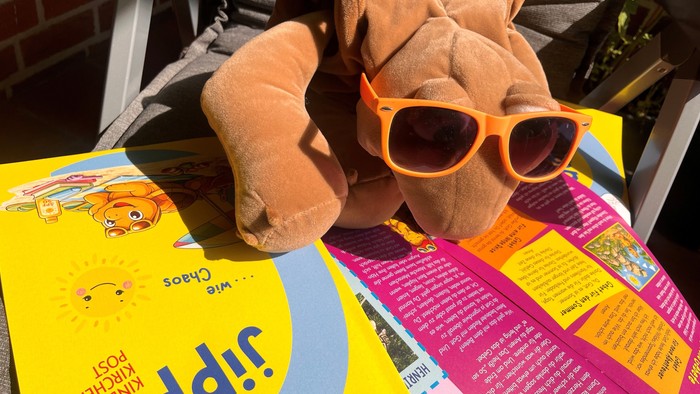 Man sieht die Handpuppe Chili aus der Kinderkirchenpost mit Sonnenbrille, wie sie in der aktuellen Ausgabe der Jippie liest.
