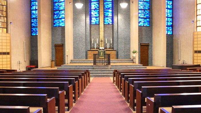 Ein Blick in die Gustav Adolf Kirche in Berlin mit rötlichem Teppich, braunen Bänken, blauen Fenstern, Kanzel und Altar