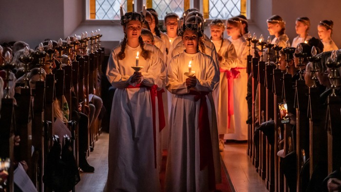 En gruppe kvinder i hvide kler og kroner står i en kirke og holder lys.