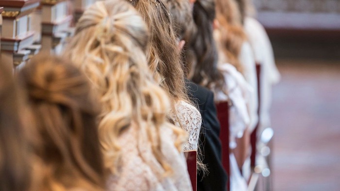 En gruppe brudepiger i formelt tøj sidder opmærksomt i en kirke under en ceremoni.