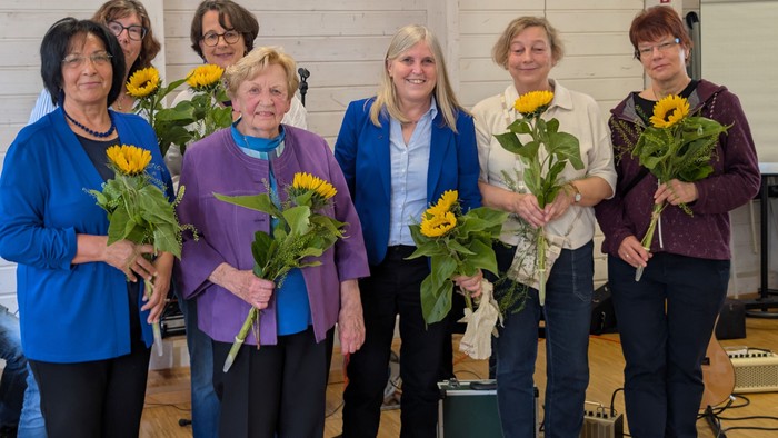 Gruppe von Menschen, die Sonnenblumensträuße in einer fröhlichen Innenraumkulisse halten.