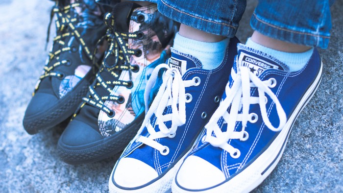 Par blå Converse-sneakers med blå jeans og farverige sokker parret ved siden af slidte sneakers.