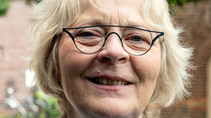 Eine etwa 60 Jahre alte Frau mit blonden, halblangen Haaren und einer schwarzen Brille schaut direkt in die Kamera.