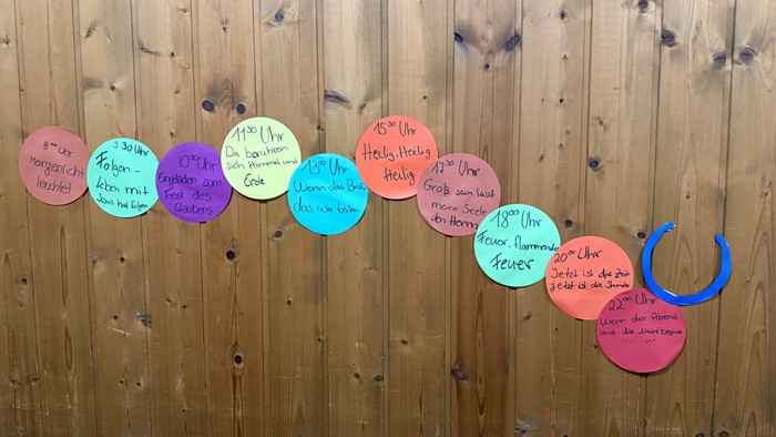 Bunte kreisförmige Notizen mit deutschen Sätzen und Uhrzeiten, angeordnet an einer Holzwand.
