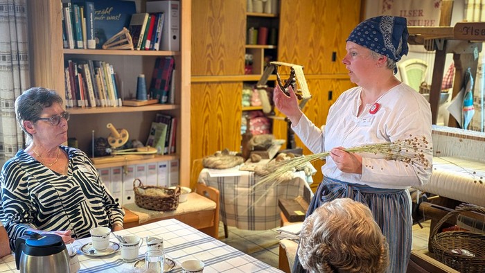 Eine Frau in Tracht zeigt einer kleinen Gruppe Leinfasern