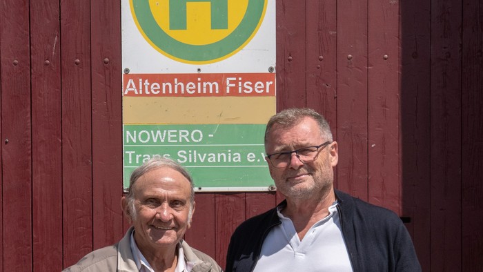 Karl Hellwig und Johan Stefani stehen an einer Bushaltestelle. Auf dem Schild steht 
