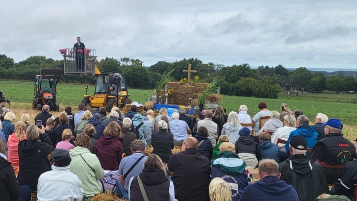 Eine große Menschenmenge versammelt sich auf einem Feld und beobachtet ein traditionelles Erntedankfest mit historischen Maschinen und Heuballen.