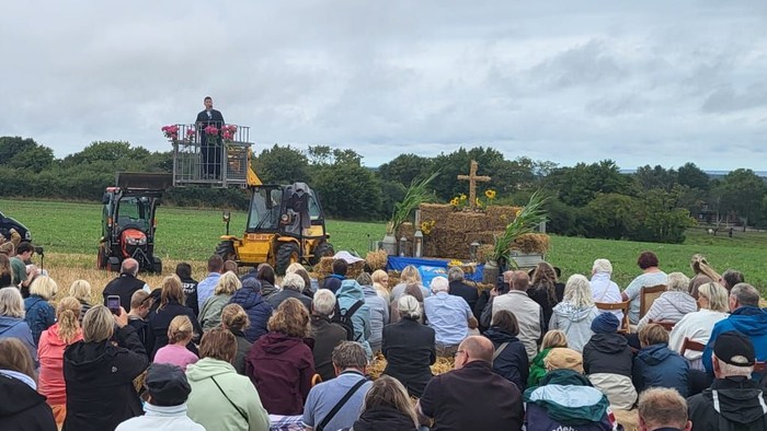 Eine große Menschenmenge versammelt sich auf einem Feld und beobachtet ein traditionelles Erntedankfest mit historischen Maschinen und Heuballen.