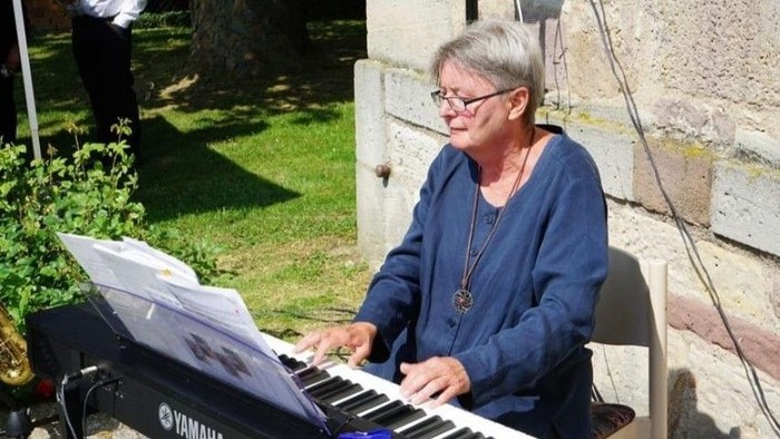 Eine Person spielt im Freien ein Keyboard in der Nähe einer Steinmauer mit aufgeschlagenen Notenblättern vor sich.