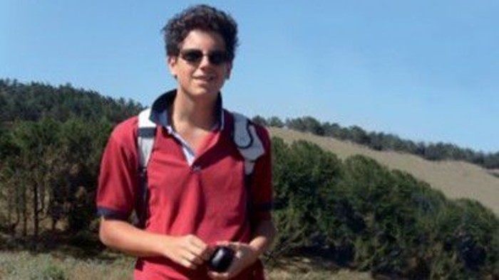 Ein junger Mann in einem roten Poloshirt hält eine Fernbedienung im Freien in einer malerischen, ländlichen Landschaft.