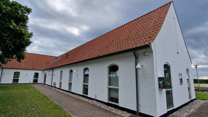 Et hvidt hus med rødt tag og flere vinduer, beliggende i en grøn og åben omgivelse