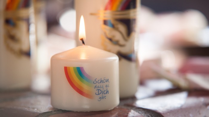 Weiße Kerze mit buntem Regenbogen und Aufschrift