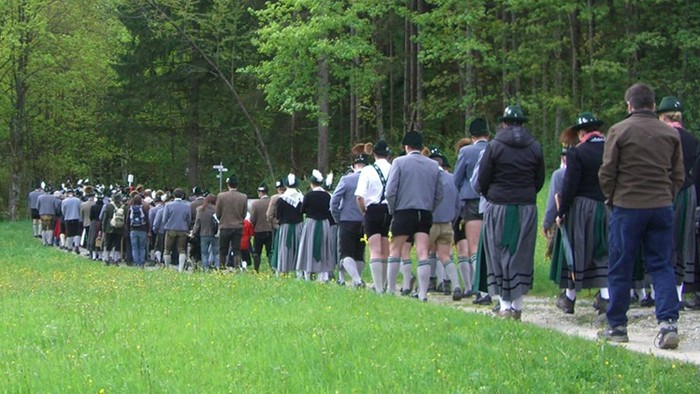 En masse mennesker går pilgrimsvandring på sti gennem skoven.