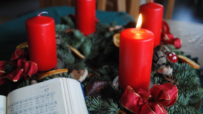 Ein Adventskranz mit einer brennenden Kerze und einem aufgeschlagenen Gesangbuch.