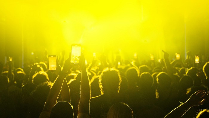 Menschen filmen Konzertmomente mit Smartphones unter hellem Bühnenlicht.