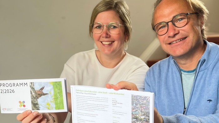 Ein Mann und eine Frau sitzen auf einer Treppe und zeigen ein Programmheft 2-2026